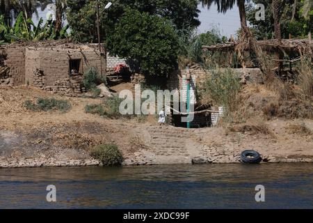 Un petit garçon égyptien descend les marches de son village de briques de boue vers le Nil un matin tandis qu'un autre regarde depuis une fenêtre. Banque D'Images