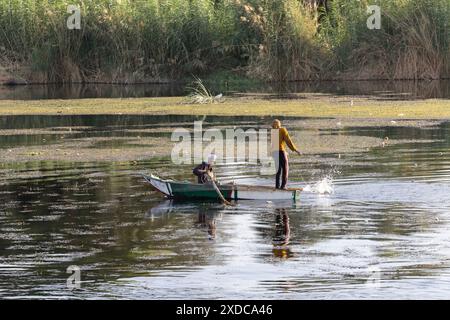 Un pêcheur souriant et son collègue pêchent en fin d’après-midi sur le Nil entre Esna et El-Kab, en Égypte, à partir de leur simple barque en bois. Banque D'Images