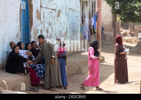 Les villageois habillés traditionnellement à Bisaw sur une île du Nil à environ 90 km au nord d'Assouan se détendent sur un banc intégré dans une rue poussiéreuse Banque D'Images