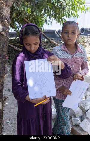 Deux écolières égyptiennes, l’une en tenue traditionnelle, l’autre en tenue moderne, montrent au photographe leurs dessins à Bisaw sur une île du Nil. Banque D'Images