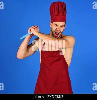 Chef mâle en colère dans le tablier Bourgogne et chapeau avec grand couteau. Homme musclé avec couteau de barbecue. Cuisine et cuisine professionnelles. Cuisson des aliments Banque D'Images