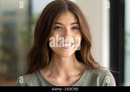 Femme souriante avec de longs cheveux bruns posant à l'intérieur, regardant la caméra Banque D'Images