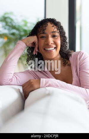 Femme souriante se relaxant sur le canapé à la maison, appuyée sur l'accoudoir Banque D'Images