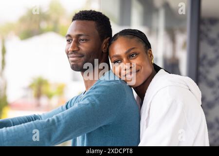 Jeune couple debout ensemble à la maison, femme embrassant l'homme par derrière, les deux souriants Banque D'Images