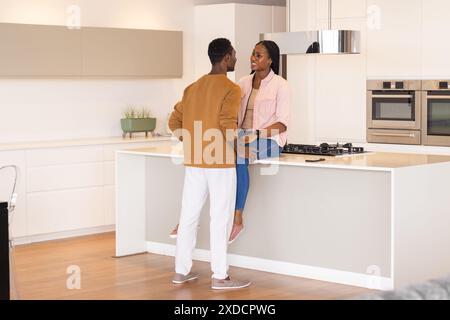 Jeune couple passant du temps ensemble dans la cuisine moderne, femme assise sur le comptoir Banque D'Images