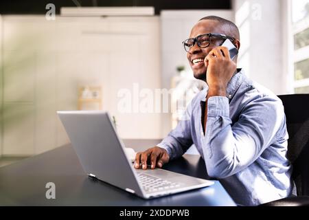 Souriant homme d'affaires afro-américain multitâche sur smartphone au bureau, communiquant avec le client pour le service de contrat RH en ligne à partir du bureau. Banque D'Images