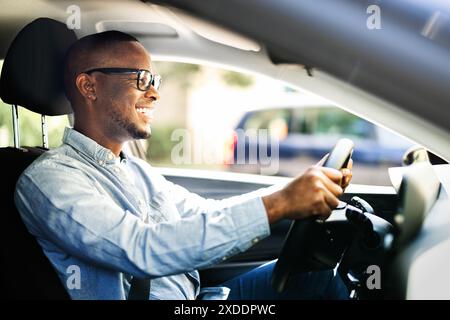PDG afro-américain prospère conduisant avec plaisir une nouvelle voiture d'entreprise en été, symbolisant la réussite et le succès dans le monde des affaires. Banque D'Images