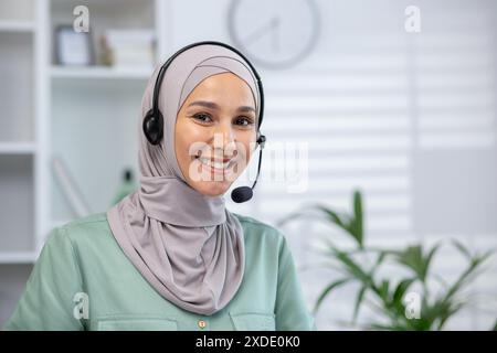 Portrait en gros plan d'une jeune femme musulmane portant le hijab et un casque debout au bureau, regardant et souriant à la caméra. Banque D'Images