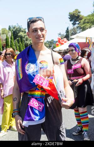 Haïfa, Israël 21 juin 2024, jeune homme portant un drapeau arc-en-ciel avec des autocollants - nous sommes ici, nous sommes queer. Banque D'Images