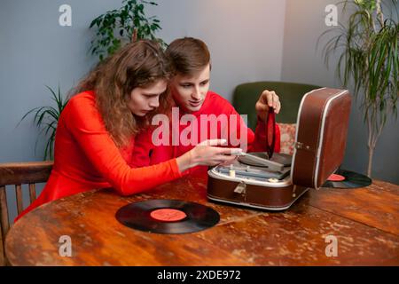Un homme et une femme sont assis à une table en bois avec un tourne-disque vintage placé devant eux. L'homme semble ajuster le tonearm, whil Banque D'Images