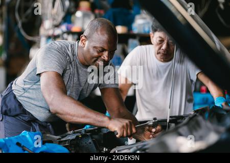 Les hommes de l'équipe de mécanicien travaillant ensemble pour réparer le problème de moteur dans l'atelier d'auto de voiture Banque D'Images