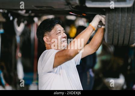 Heureux mécanicien asiatique travaillant véhicule de réparation dans le service de voiture. Système de suspension de fixation pour travailleurs sous véhicule. Banque D'Images