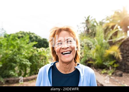 Heureuse femme latine senior souriant à la caméra tout en marchant dans un parc public Banque D'Images