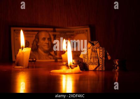 Une chemise avec un billet d'un dollar et une pile de pièces de monnaie se tiennent sur une armoire en bois contre la toile de fond des dollars à la lueur des chandelles dans l'obscurité, les affaires et les ailerons Banque D'Images