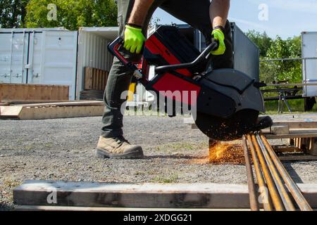 Un homme avec une grande meuleuse en acier coupe des barres de renfort en acier sur un chantier de construction Banque D'Images