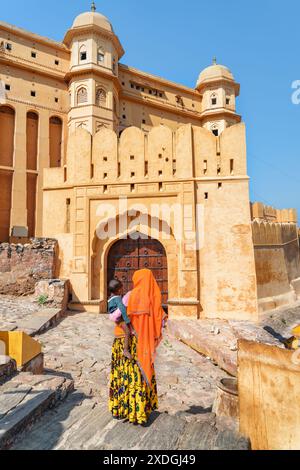 Jaipur, Inde - 12 novembre, 2018 : femme indienne inconnue portant un sari coloré traditionnel tenant l'enfant sur fond de porte scénique. Banque D'Images