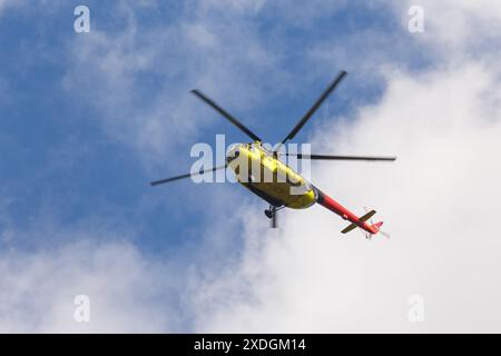 Hélicoptère Mi-8 jaune-orange en vol sur fond d'un ciel bleu avec des nuages Banque D'Images