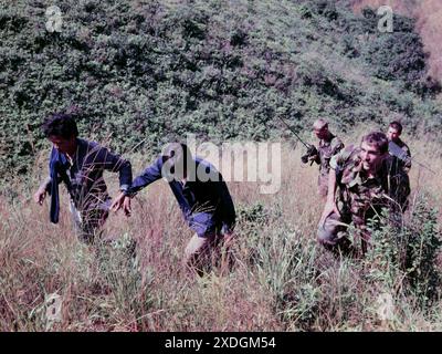 Deux hommes immigrés clandestins (« IIS »), qui viennent d'être arrêtés à Hong Kong, sont escortés jusqu'à Robin's Nest, une colline près de la frontière dans les nouveaux Territoires de Hong Kong, par deux soldats du régiment de Cheshire de l'armée britannique. Oct 1984. Le soldat de gauche porte un coffret radio à l'ancienne. Banque D'Images