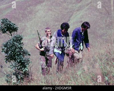 Deux hommes immigrés clandestins (« IIS »), qui viennent d'être arrêtés à Hong Kong, sont escortés jusqu'à Robin's Nest, une colline près de la frontière dans les nouveaux Territoires de Hong Kong, par deux soldats du régiment de Cheshire de l'armée britannique. Oct 1984. Le soldat de gauche porte un coffret radio à l'ancienne. Banque D'Images