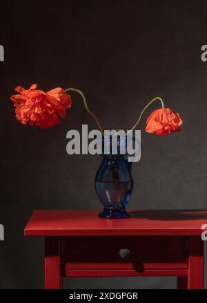 2 coquelicots dans un vase bleu sur une table de chevet Banque D'Images