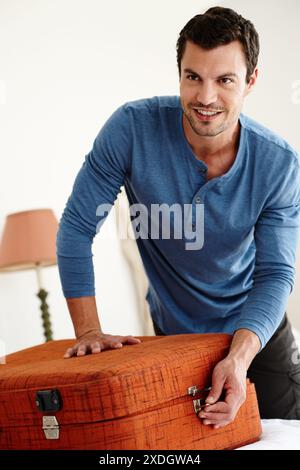 Homme, emballage et valise sur le lit à l'hôtel pour le voyage, les vacances et l'été comme personne prête en Espagne. Touriste, sourire et bagages ou sac dans la chambre pour Banque D'Images