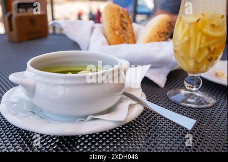 Dîner à la table du restaurant, soupe aux épinards dans un bol blanc, boisson au gingembre dans un verre et deux petits pains. Banque D'Images