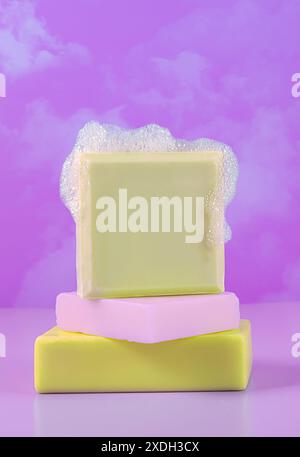 Barres de savon jaunes et violettes avec de la mousse, empilées, ciel rose avec fond de nuage Banque D'Images