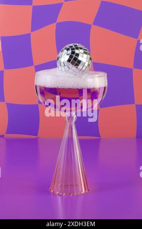 Boule disco moderne dans un verre de champagne de bain à bulles, fond carrelé orange ondulé et violet vif Banque D'Images