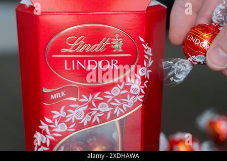 La main d'un homme prenant une truffe au chocolat Lindor dans une boîte de chocolat Lindt rouge. Chocoladefabriken Lindt & Sprüngli AG, exerce ses activités sous le nom de Lindt Banque D'Images