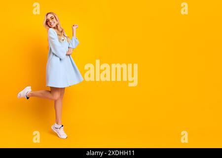 Femme souriante en robe bleue posant sur fond jaune Banque D'Images