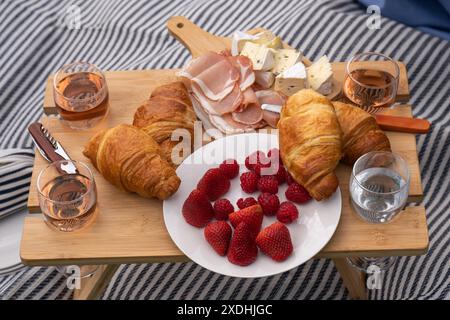 Une petite table servie avec de la nourriture pique-nique se dresse sur une clairière verte dans un parc de la ville. Fraises, croissants, fromage, collations, vin pique-nique en plein air, variou Banque D'Images