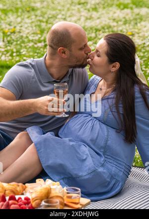 Heureux couple enceinte passant du temps ensemble sur un pique-nique en plein air. Un tendre baiser des futurs parents. La famille attend un enfant. Grossesse Banque D'Images