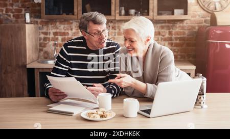 Couple senior examinant les documents ensemble dans la cuisine Banque D'Images