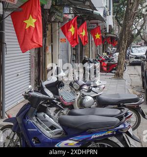 Hanoi, Vietnam - 9 février 2024 : scooters à moteur alignés sous les drapeaux du Vietnam dans la vieille ville de Hanoi Banque D'Images