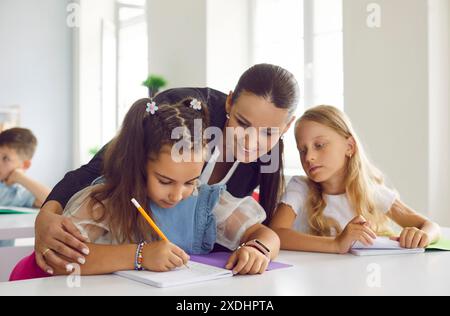 Enseignante préoccupée aidant les petites écolières à prendre des leçons en classe à l'école primaire. Banque D'Images