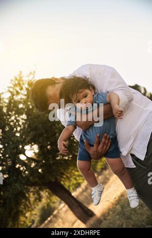 Un père tenant la main de son fils d'un an alors que le garçon court sur l'herbe, tous deux profitant d'un moment joyeux à l'extérieur Banque D'Images