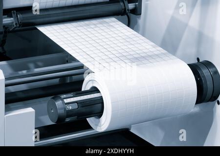 Un rouleau de papier blanc est passé dans la machine. imprimante et machine à autocollants, qui est utilisée pour imprimer et appliquer des autocollants à l'indust d'emballage Banque D'Images