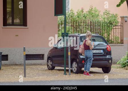 Cremona, Italie - 21 juin 2024 femme isattend à l'arrêt de bus dans un quartier résidentiel avec des arbres et un bâtiment en arrière-plan sur un da d'été ensoleillé Banque D'Images