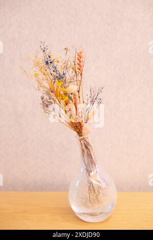 bouquet de fleurs sèches et d'herbes dans un vase en verre sur fond de mur. Nature morte dans un style rustique. Lumière dure. Carte postale avec place pour le texte. Banque D'Images