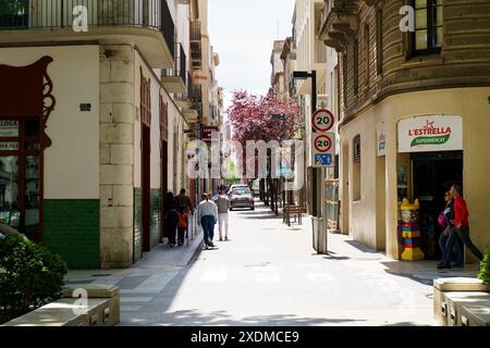 Figueres, Espagne - 14 mai 2023 : une rue encombrée de la ville avec des piétons marchant vigoureusement. Le sentier étroit est bordé de bâtiments des deux côtés. Banque D'Images