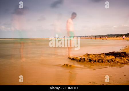 Photographie longue exposition capturant la plage sereine et historique d'Omaha en Normandie, France avec des figures floues par une journée calme. Banque D'Images