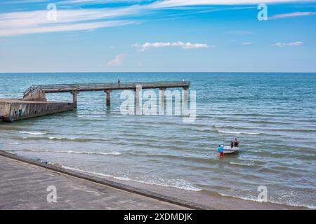 Journée calme à Omaha Beach en Normandie, France, avec un quai serein et un petit bateau flottant sur de douces vagues. Banque D'Images