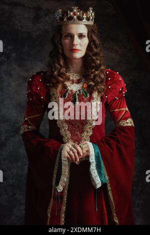 reine médiévale en robe rouge avec couronne sur fond gris foncé. Banque D'Images