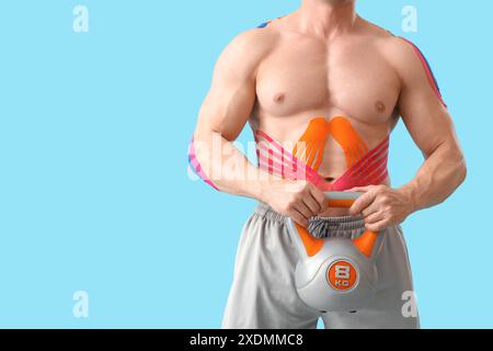 Jeune homme musclé avec physio tape et kettlebell sur fond bleu, gros plan Banque D'Images