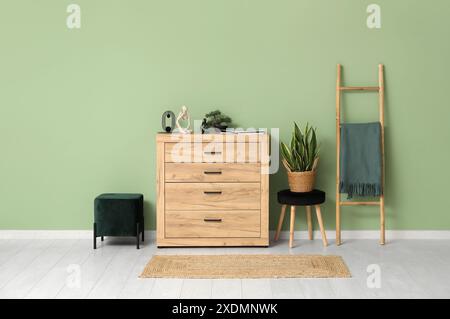 Commode en bois près de la chaise avec plante d'intérieur et pouf dans la chambre Banque D'Images