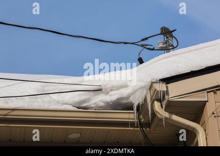 Mât de service de ligne électrique résidentiel sur le toit avec des câbles enveloppés dans la glace et la neige en hiver. Banque D'Images