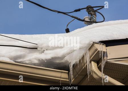 Mât de service de ligne électrique résidentiel sur le toit avec des câbles enveloppés dans la glace et la neige en hiver. Banque D'Images