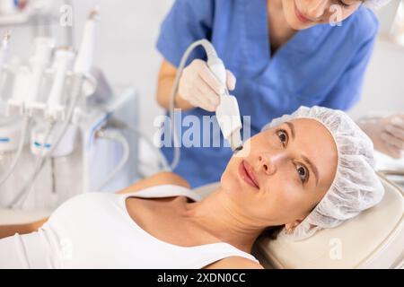 Jeune patiente subissant un nettoyage de la peau du visage avec une pelle ultrasonique Banque D'Images