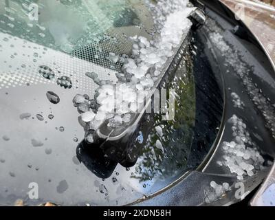 Gros plan d'un pare-brise de voiture couvert de grêle et de gouttes de pluie, mettant en évidence les conséquences d'une tempête de grêle avec des granulés de glace accumulés autour de la wi Banque D'Images