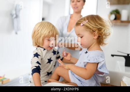 Routine de salle de bain du matin pour les petits enfants. Fille peignant ses ongles, frère regardant. Banque D'Images